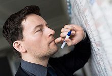 Mann trägt Termine in einen Wandkalender ein - Alexander Heinl/dpa-tmn