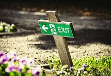FOTOMONTAGE, Schiefes Holzkreuz mit Fluchtweg-Schild, Symbolfoto Kirchenaustritte *** PHOTOMONTAGE, crooked wooden cross - IMAGO/Christian Ohde