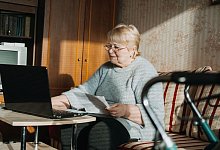 Life Insurance, Disability medical insurance policy for Seniors. Mature woman in glasses with Laptop and documents on the background of Rollator Mobility Walker for Seniors at home. - Verbraucherzentrale NRW