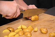 Koch schneidet mit Küchenmesser rohe Kartoffeln in Spalten - Nahaufnahme - picture alliance / CHROMORANGE
