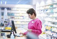 Smiling pharmacist with medical prescription using computer at desk - picture alliance / Westend61