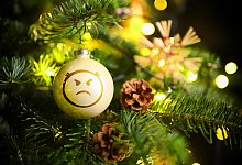 Weihnachtskugel mit Wut-Emoji h&auml;ngt an einem Weihnachtsbaum, Symbolfoto Streit unterm Weihnachtsbaum, Fotomontage - picture alliance / CHROMORANGE