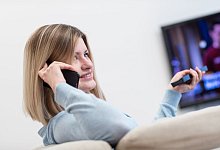 Gleichzeitig TV schauen und telefonieren &uuml;ber einen Vertrag - Foto: Christin Klose/dpa-tmn