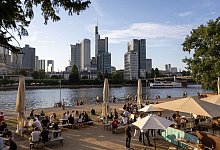 Menschen sitzen in einem Cafe am Mainufer, im Hintergrund die Skyline. In der Gastronomie gibt es unter anderem wegen der Pandemie einen großen Personalmangel. - Hannes P. Albert/dpa