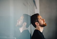 Ein junger Mann lehnt nachdenklich an einer Glaswand - Zacharie Scheurer/dpa-tmn