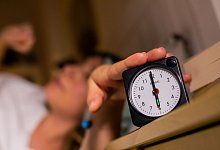 Eine Frau schaltet vom Bett aus einen auf sechs Uhr gestellten Wecker aus. - Christoph Soeder/dpa/Illustration