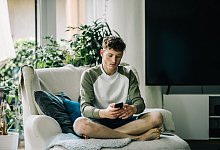 Ein junger Mann sitzt mit Smartphone auf einem Sessel - Zacharie Scheurer/dpa-tmn