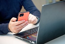 Ein Mann nutzt ein Handy am Laptop - Zacharie Scheurer/dpa-tmn