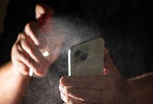 Mann reinigt sein Smartphone mit einem Spray - Franziska Gabbert/dpa-tmn