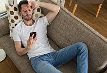 Genervter Smartphonenutzer auf Sofa - Christin Klose/dpa-tmn