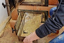 Eine Frau entnimmt die Ascheschublade aus einem Kachelofen - Monique Wüstenhagen/dpa-tmn