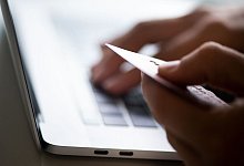 Eine Person sitzt am Laptop und hält eine Bankkarte in der Hand. - Franziska Gabbert/dpa-tmn/Symbolbild