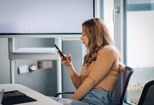 Eine Frau blickt auf ihr Smartphone in einem Konferenzraum - Zacharie Scheurer/dpa-tmn