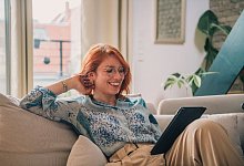 Eine Frau sitzt auf einer Couch und bedient ein Tablet - Zacharie Scheurer/dpa-tmn