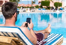 Mann mit Smartphone am Hotelpool - Benjamin Nolte/dpa-tmn/dpa