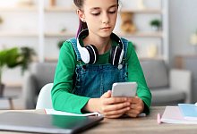 Girl sitting at desk, chatting on cell phone, reading message - IMAGO/YAY Images