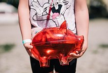 Ein Kind trägt ein rotes Sparschwein - Zacharie Scheurer/dpa-tmn