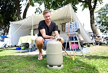 Mann schließt eine Gasflasche an einen Grill an - Tobias Hase/dpa-tmn