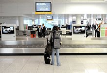 Ein Passagier wartet am Laufband auf seinen Koffer - Tobias Hase/dpa-tmn