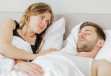 Frau betrachtet schnarchenden Mann im Bett - Monique Wüstenhagen/dpa-tmn