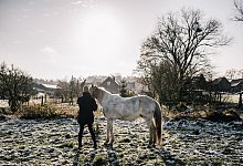 Ein Mensch und ein Pferd drau&szlig;en auf einer Wiese im Winter. - Zacharie Scheurer/dpa-tmn