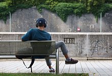 Junger Mann sitzt mit Kopfhörer auf einer Bank - Karl-Josef Hildenbrand/dpa/dpa-tmn
