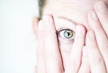 Frau schaut &auml;ngstlich zwischen ihren Fingern hervor - Franziska Gabbert/dpa-tmn