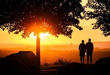 Ein Paar steht bei Sonnenaufgang auf einem Berg - Julian Stratenschulte/dpa/dpa-tmn