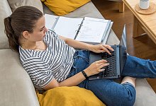 Eine Frau sitzt mit Laptop und Aktenordnern auf einem Sofa - Christin Klose/dpa-tmn