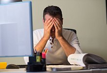 Mann stützt an seinem Schreibitsch den Kopf in seine Hände - Klaus-Dietmar Gabbert/dpa-tmn