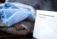 Liefer- und Retourenschein liegt neben online bestellter Kleidung - Sina Schuldt/dpa/dpa-tmn