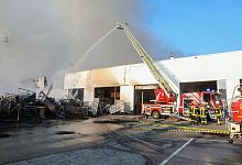 Einsatzkräfte der Feuerwehr stehen während eines Großbrandes auf dem Gelände des Reifengroßhändlers und löschen das Feuer. - Thomas Warnack/dpa