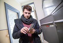 Mann öffnet Brief an einem Briefkasten im Hausflur - Christin Klose/dpa-tmn