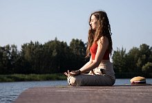 Frau meditiert am See - Christin Klose/dpa-tmn