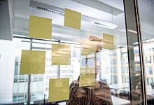 Eine Frau klebt Post-its an eine Glaswand - Zacharie Scheurer/dpa-tmn/dpa