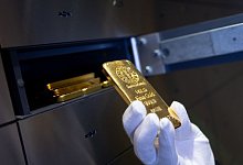 Mann legt einen Goldbarren in ein Schlie&szlig;fach eines Tresorraums - Sven Hoppe/dpa/dpa-tmn