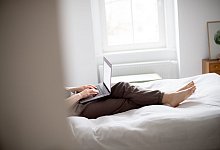 Eine Frau sitzt mit Laptop im Bett - Zacharie Scheurer/dpa-tmn