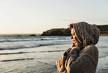 Eine Frau steht bei Sonnenuntergang am Strand - Uwe Umstätter/Westend61/dpa-tmn