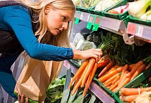 Eine Frau wählt Karotten aus dem Regal aus - Benjamin Nolte/dpa-tmn
