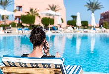 Frau telefoniert am Hotelpool - Benjamin Nolte/dpa-tmn