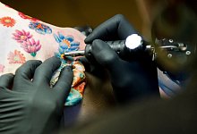 Tätowierer sticht ein Tattoo auf dem Rücken einer Kundin - Franziska Gabbert/dpa-tmn