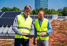 Zwei Arbeiter stehen auf dem begr&uuml;nten Dach vor einer Solaranlage - Daniel Ingold/Westend61/dpa-tmn