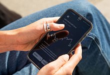 Eine Frau sieht sich einen ETF-Kurs auf einem Handy an - Christin Klose/dpa-tmn