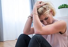 Junge Frau sitzt traurig auf dem Fußboden einer Wohnung - Christin Klose/dpa-tmn