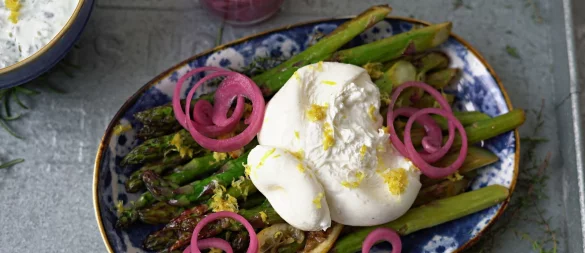 Zum Anrichten wird der Burrata über den Spargelstangen etwas auseinander gezupft und mit dem Ranchdip beträufelt. Zuvor eingelegte rote Zwiebelringe bringen Farbe auf den Teller. - © Mareike Pucka/biskuitwerkstatt.de/dpa-tmn