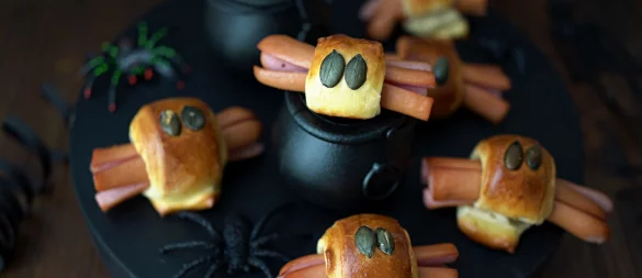 Für die Würstchenspinnen werden die an den Enden eingeschnittenen Wienerstückchen mit Teigstreifen umwickelt. Darauf drückt man je zwei Kürbiskerne als Augen und schiebt das Ganze in den Backofen. - © Mareike Pucka/biskuitwerkstatt.de/dpa-tmn
