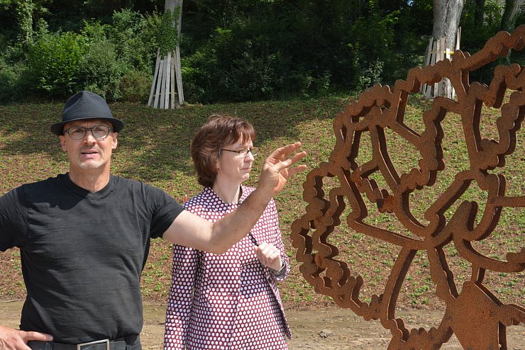 Künstler Hans Kordes zeigt die Patina an dem kleineren Stahlkunstwerk. Auch die „größte Nelke der Welt" wird in knapp einem Jahr über eine identische Oberfläche verfügen. Im Hintergrund ist Kathrin Ridder, Vorsitzende von Blomberg Marketing, zu sehen. Sie stellte den Antrag den Vattipark in „Nelkenpark" umzubenennen. - © Tanja Watermann
