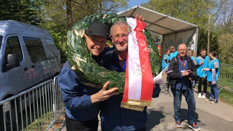 Da war die TSVE-Welt noch in Ordnung: Orgateam-Mitglieder Matthäus Gruben (l.) und Rudi Ostermann erlauben sich im Zielbereich einen Spaß mit dem Kranz während sie auf die schnellsten Läufer und Läuferinnen warten. - © Stephanie Fust