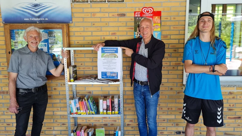 Wolfgang Kohl und Peter Schindel vom F&ouml;rderverein der Stadtbibliothek Detmold &uuml;bergeben das gespendete B&uuml;cherregal in Berlebeck an Toni Lause, Fachangestellter f&uuml;r B&auml;derbetriebe (von links). - &copy; Stadt Detmold