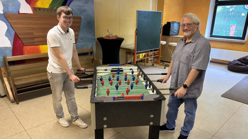 Tim Alexander (links) und Axel Schwarze laden Kinder und Jugendliche zum Mitmachen ein. Hier stehen sie am Kicker in der Trinitatiskirche in Schötmar. - © Sven Kienscherf